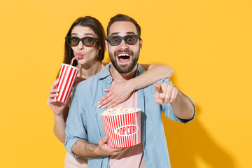 Amazed young couple friends guy girl in 3d glasses isolated on yellow background. People in cinema...