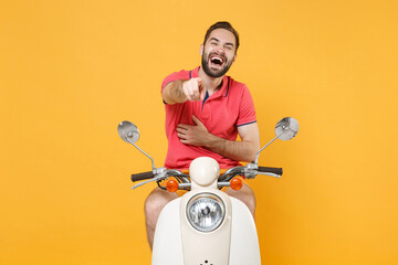 Laughing young bearded man guy in casual summer clothes driving moped isolated on yellow background. Driving motorbike transportation concept. Pointing index finger on camera, put hand on stomach.