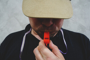 coach in a cap blows in a red whistle close-up
