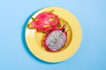 Cut dragon fruit in a yellow plate. Under pitaya with seeds on a colored background. Top view, flat layout