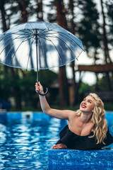 Pretty pin up styled blonde in black vintage swimsuit relaxing in the swimming pool