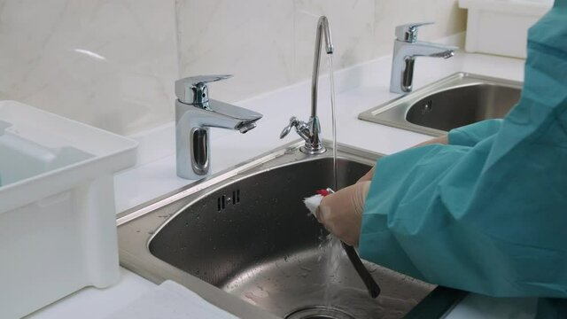 Medium shot of Doctor in white gloves wash dental tools under a stream of distilled water from the tap and puts them on a clean towel. Before the disinfection procedure of orthodontic pliers.