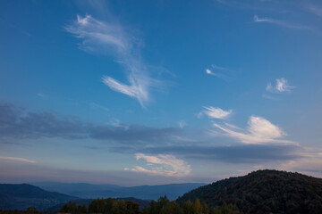 Beautiful white clouds on a background of blue sky. Landscape in the mountains. Sunset sky. Orange sunset.