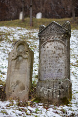 Gray and brown gravestones in an old Jewish cemetery in the Carpathian mountains. Hebrew inscriptions on tombstones. Jewish cemetery in the winter in the snow.