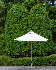 One outdoor white fabric umbrella on a patio with green shrubs in the background.