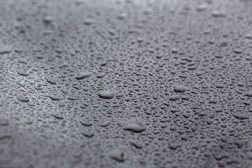 Drops of water on a black metal surface. Selective focus in center.