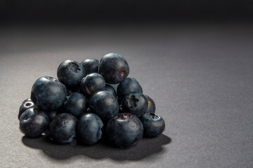 Close up on natural and organic blueberry fruits stacked to a pyramid shape. Light falls from behind on dark background