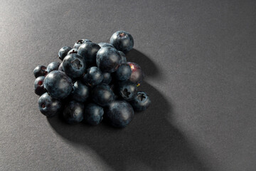 Close up on natural and organic blueberry fruits stacked to a pyramid shape. Light falls from behind and creates shadow on dark background with space for text