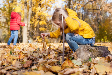 Children hiking in the forest. Girls exploring nature in the woods on autumn day, sitting on rock and playing with stick and leaves Outdoor recreation and family awesome adventures with kids in fall