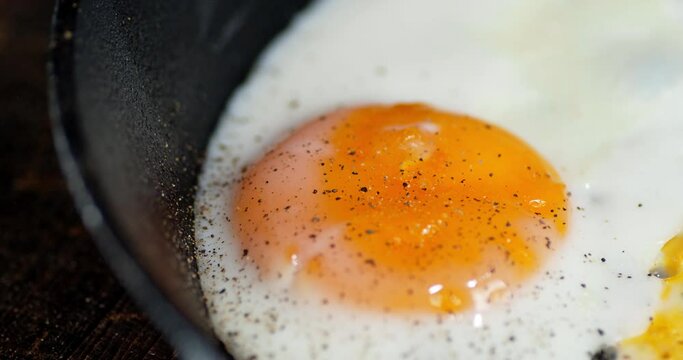Fried egg in a frying pan strewed ground black pepper.