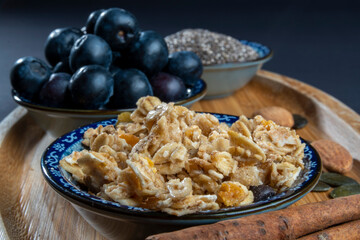 Healthy/natural food concept: On wooden board, some cinnamon sticks, almonds and sunflower seeds. Close up on crunchy granola, blueberries and chia seeds