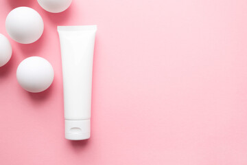 Cream lotion container tube and white ping pong balls on cute pink background. Abstract with geometric sphere shapes and copy space for text. Concept delicacy, lightness and pure skincare