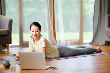 Beautiful women doing yoga by lie down and look example from laptop also she look happy and relax. Concept of workout at home for good health and prevent virus infection of pandemic.