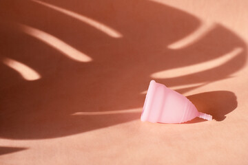 Menstrual cup on a pink background with the shadow of a tropical palm leaf. The concept of critical days during the holidays and summer