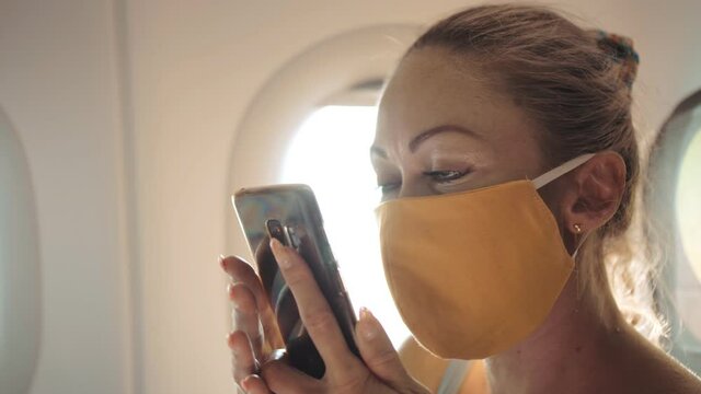 Woman travel tourist caucasian at plane aircraft with wearing protective medical mask. Girl talking about coronovirus on phone smartphone mobile. Virus epidemic sars-cov-2 covid-19 2019-ncov.