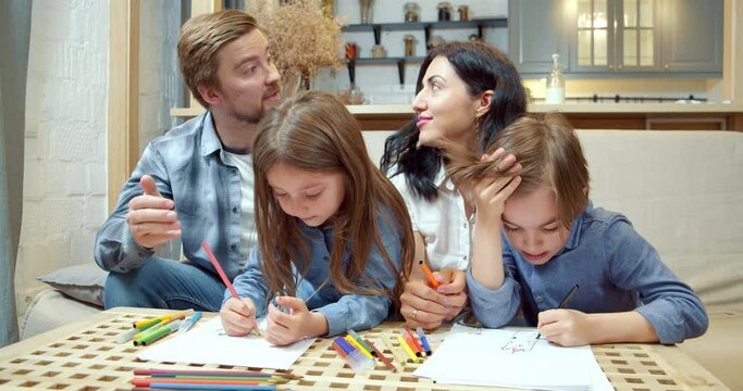 Happy creative family with two cute children drawing with colored pencils and markers on paper together sitting on the sofa at home.