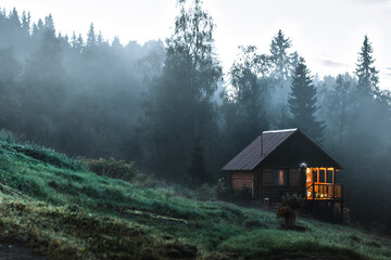 Small old wooden house in foggy forest. Mountains scenery. Nature conceptual image.