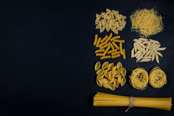 Assorted types of pasta on black background. Top view. Various forms of pasta. Copy space for design.