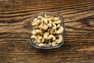 Cashew nuts in a small plate on a vintage wooden table as a background. Cashew nut is a healthy vegetarian protein nutritious food.