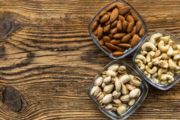 Almond, pistachio and cashew in a small plates which standing on a wooden vintage table. Nuts is a healthy vegetarian protein and nutritious food. Nuts on rustic old wood.