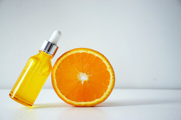 Cosmetic bottle with Vitamin C serum and half of orange on white background. Citrus essential oil, cosmetics aromatherapy. Organic SPA cosmetics with herbal ingredients.