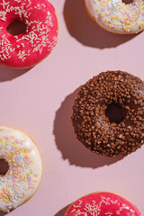Chocolate, pink and vanilla donuts with sprinkles, sweet glazed dessert food on pink minimal background, top view