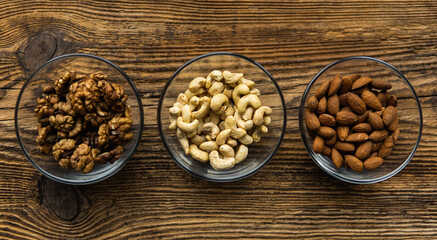 Almond, walnut and cashew in a small plates which standing on a wooden vintage table. Nuts is a healthy vegetarian protein and nutritious food. Nuts on rustic old wood.