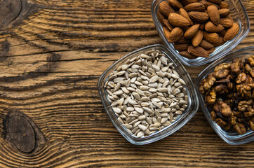 Almond, walnut and sunflower seeds in a small plates which standing on a wooden vintage table. Nuts is a healthy vegetarian protein and nutritious food. Nuts on rustic old wood.