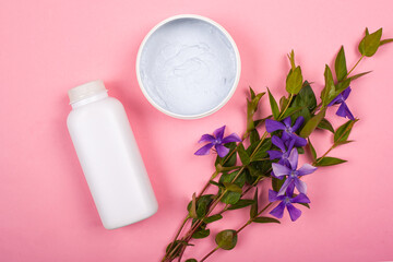 Obraz na płótnie Canvas skin care cosmetics, beauty, white bottles on a pink background with branches of purple wildflowers
