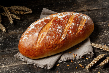 Loaf of white bread on textile towel on rustic wooden texture background