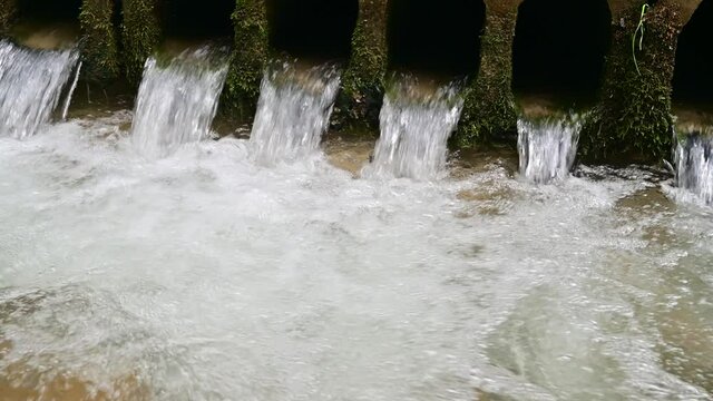 Water flows through pipes inder an old bridge
