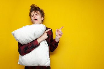 sleepy tired guy yawns, holds a pillow on yellow isolated background and shows at copyspace, bad morning, insomnia concept