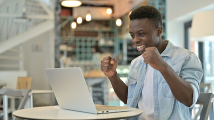 Positive Young African Man Celebrating Success on Laptop in Cafe
