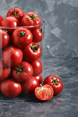 Medium red tomatoes with a glass vase on a gray background. Copy space, abstraction, fresh vegetables.