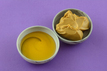 Peanut butter and honey in grey dipping bowls on purple background