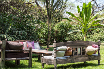 Outdoor furniture with sofas, pillows and a table in the center, in a relaxing atmosphere in a backyard among green trees.
