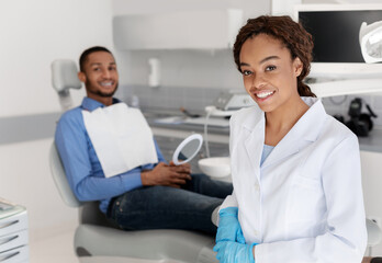 Smiling dentist and patient looking at camera, dental cabinet interior