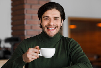 Portrait of cheerful man drinking tea or coffee at cafe