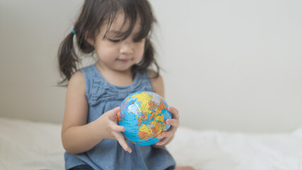 Happy playful toddler looking at globe ball on bed in bedroom at home.