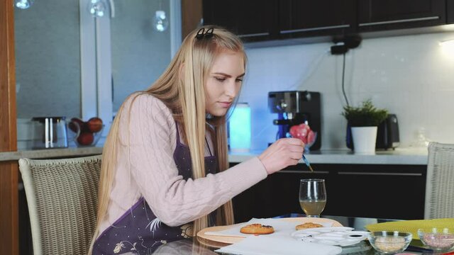 Beautiful woman painting sweet cookies with special food colors in the kitchen. Cooking traditions concept.