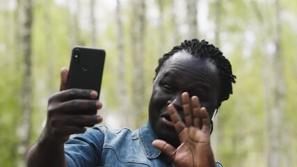 An african man using smartphone for a video call. Waving to his family from the forest. - Powered by Adobe