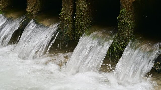 Water flows through pipes inder an old bridge
