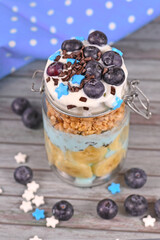 Obraz na płótnie Canvas Blueberry snack made from yogurt and banana and healthy fruits topped with star shaped sugar and chocolate sprinkles in jar on wooden background