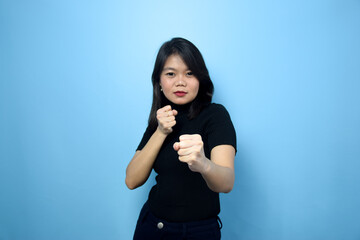 Fototapeta premium Portrait of Young beautiful asian women wearing black turtle neck shirt with blue isolated background, Punching fist to fight, Fight Gesture Concept