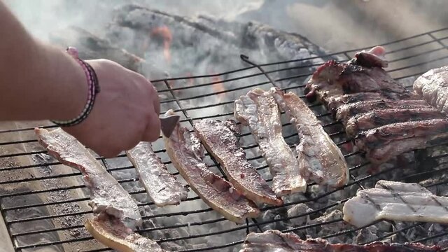 Una mano de un chico cocinando panceta sobre una parrilla sobre el fuego 
