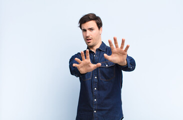 young handsome man feeling terrified, backing off and screaming in horror and panic, reacting to a...
