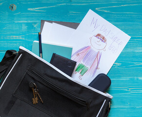 Men's briefcase with papers and children's drawing with the signature my dad is a super hero, blue background with space