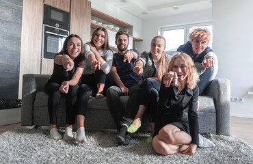 Group of young smiling people in the sofa pointing at camera