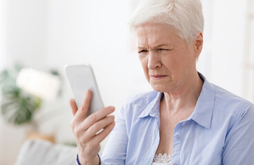 Fototapeta na wymiar Myopia Concept. Elderly woman squinting while looking at smartphone screen