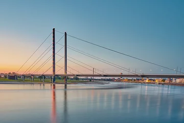 A cable-stayed bridge that leads across the Rhine. It is evening and the lighting of the bridge and the city of Düsseldorf are noticeable.     © Bastian